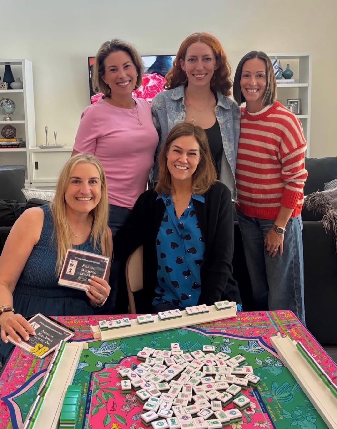 Shauna with a group of students around the table at a Las Vegas Mahjong lesson, holding the National Mah Jongg League card