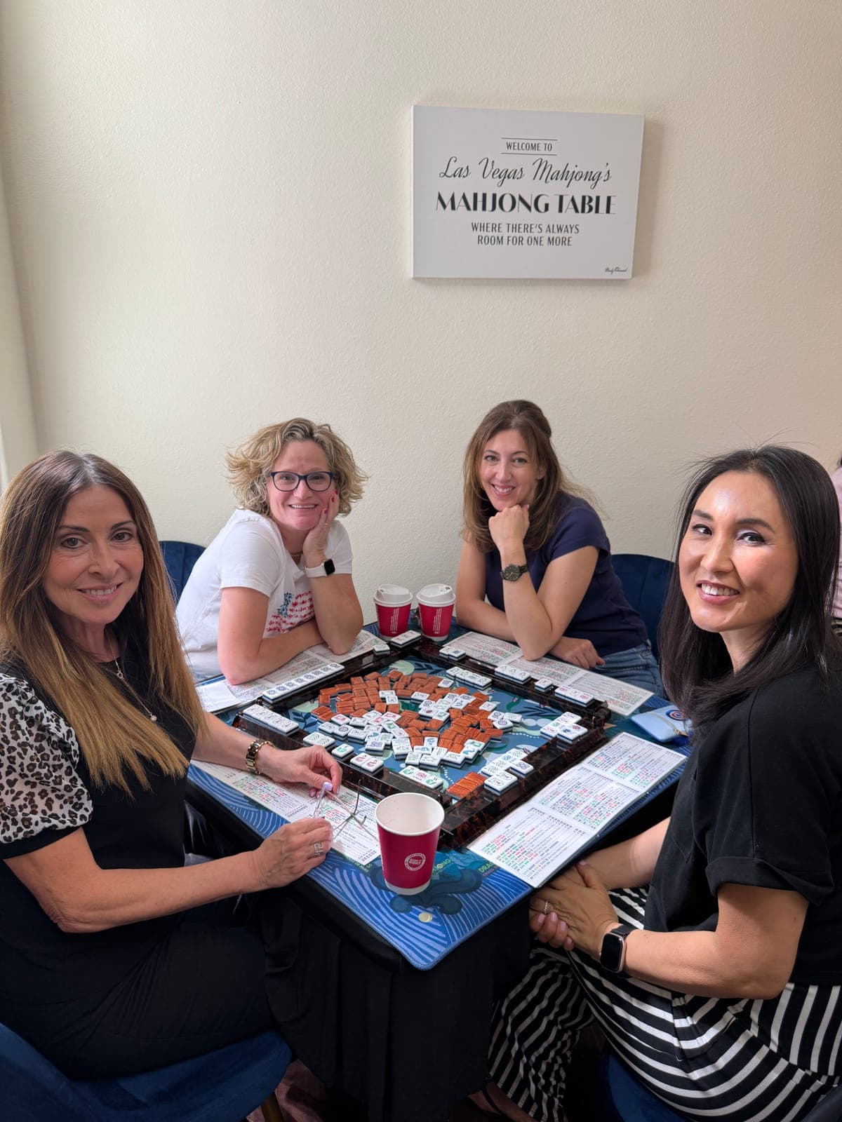 Four players smiling around a mahjong table during open play at the Las Vegas Mahjong Studio